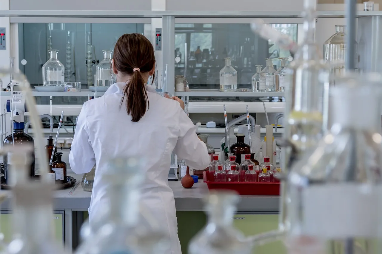 A woman in a lab coat is focused on her project, surrounded by scientific equipment and materials.